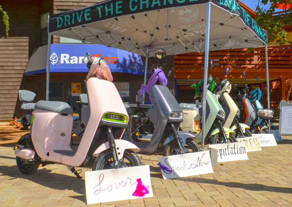 Electric scooters on display under a canopy with various signs and branding in the background.