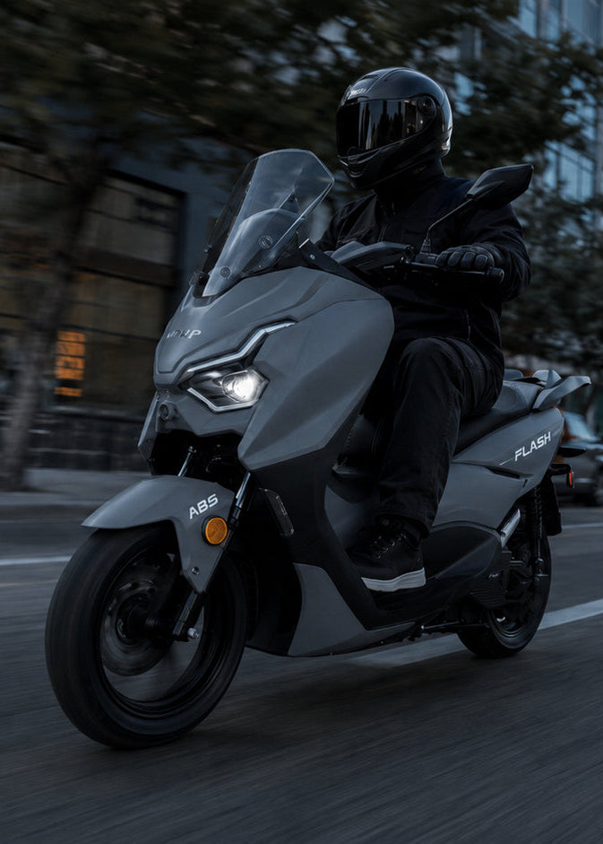 Person riding a scooter on a city street with buildings and traffic lights in the background