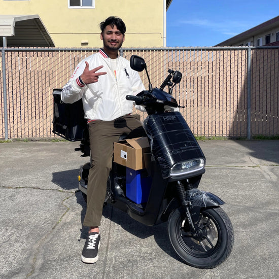 A delivery rider smiling and sitting on a black electric scooter with packages, ready for last-mile delivery.
